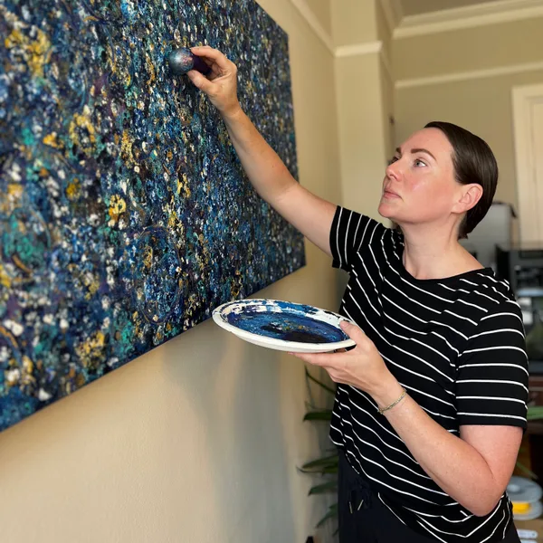 Kelly applying paint to a blue abstract artwork.