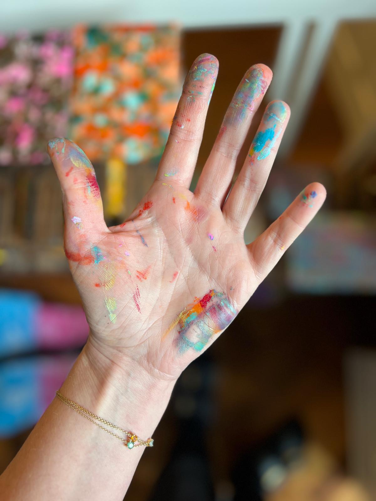 Paint-covered hand in front of colorful artwork in Kelly's Amsterdam studio.